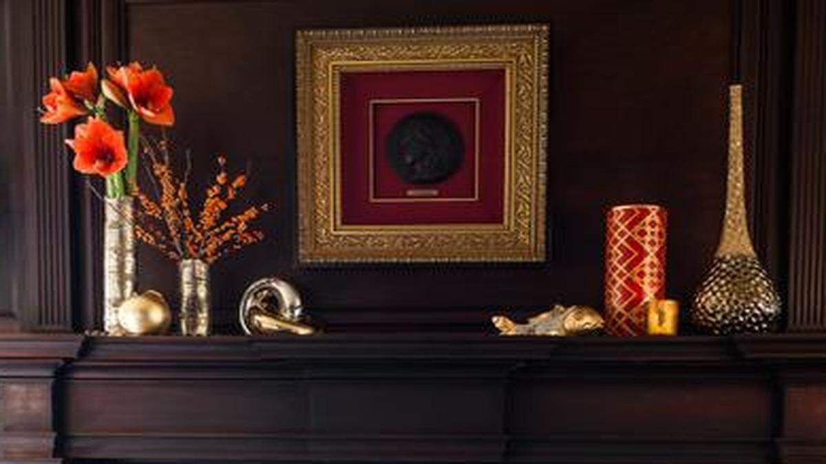 The dark wood paneling surrounding Debbie and Paul Stevermer’s living room fireplace is complemented by brass, including, on the right side of the mantel, a fish sculpture and tall vase from Alejandro Home Design; and a red vase, throw pillow and marble-top table from Madden-McFarland.