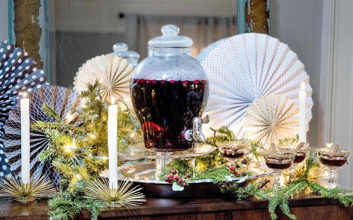 A bowl of Warm Mulled Wine, created by Affäre bar manager Chelsea Almeida, nestles in a festive display. The glass dispenser sits atop a cake stand surrounded by evergreen branches, string lights, paper fans from Paper Source ($24.95 for several in multiple sizes) and brass candleholders from Pryde’s of Westport (three sizes: $19.99, $29.99, $39.99).