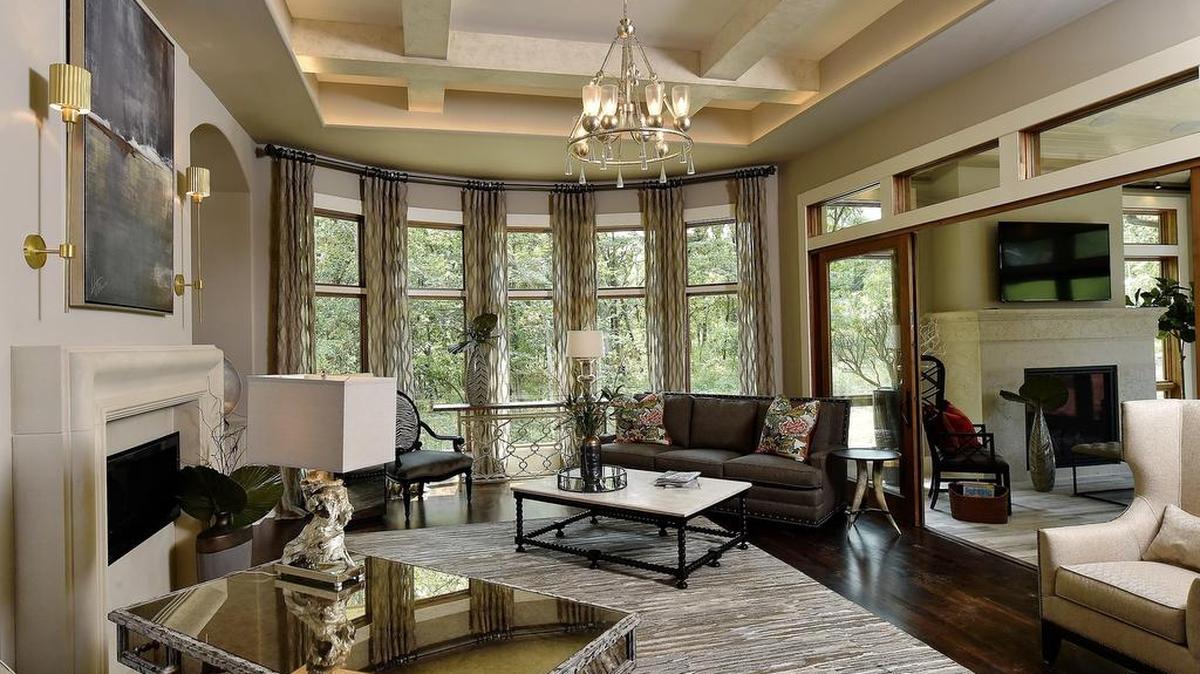 
Hidden LED lights accentuate the coffered ceiling in the living room of this Village of Loch Lloyd home by Willis Construction. The fireplace features a cast limestone mantel and a wall of mirrors to reflect a firepit, water fall and outdoor kitchen on a multi-level flagstone patio. The bowed windows offer a panoramic view of woods behind the home.
