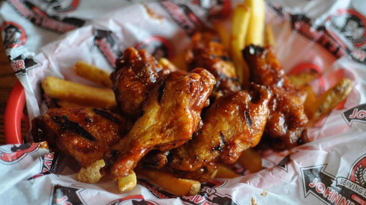 Johnny’s Tavern makes its popular Wilson Wings by frying and grilling chicken wings, then coating them in hot sauce with a hint of sweet barbecue flavor.
