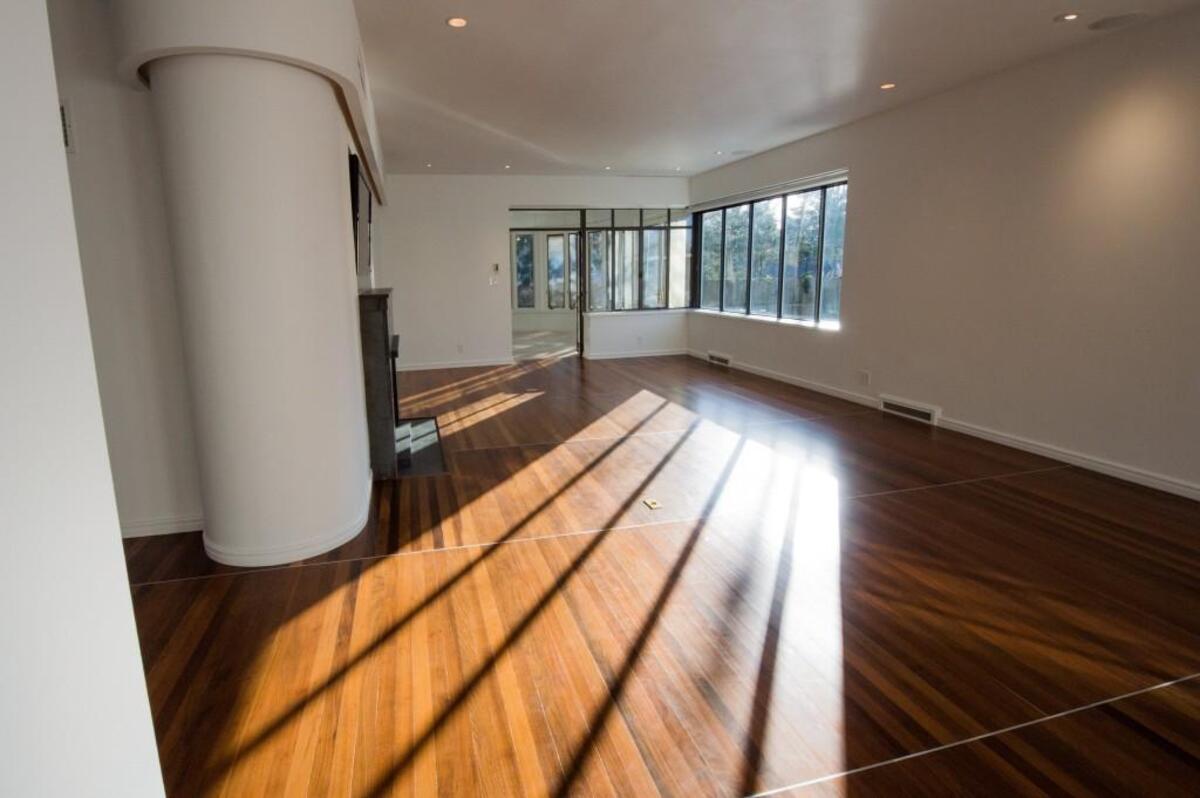 Paned windows round a corner of the living room, offering views of an in-ground swimming pool and cabana in the backyard and a semi-circular solarium on the side of the home
