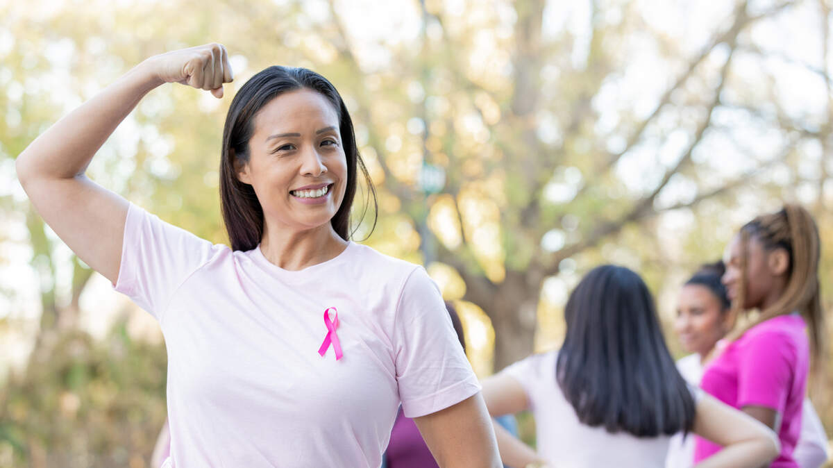 Young woman shows strength while attending breast cancer awareness fundraiser and wearing pink ribbon. 
