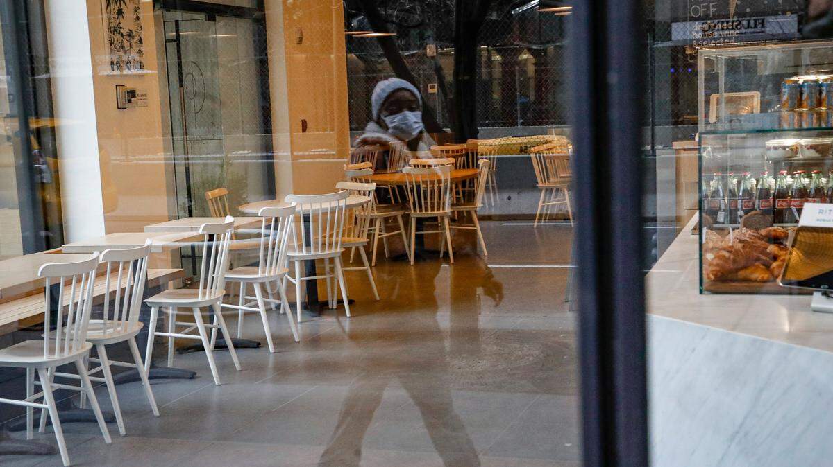 A pedestrian wearing a protective face mask walks past a nearly empty restaurant near Grand Central Terminal, Monday, March 16, 2020, in New York. New York leaders took a series of unprecedented steps Sunday to slow the spread of the coronavirus, including canceling schools and extinguishing most nightlife in New York City. (AP Photo/John Minchillo)