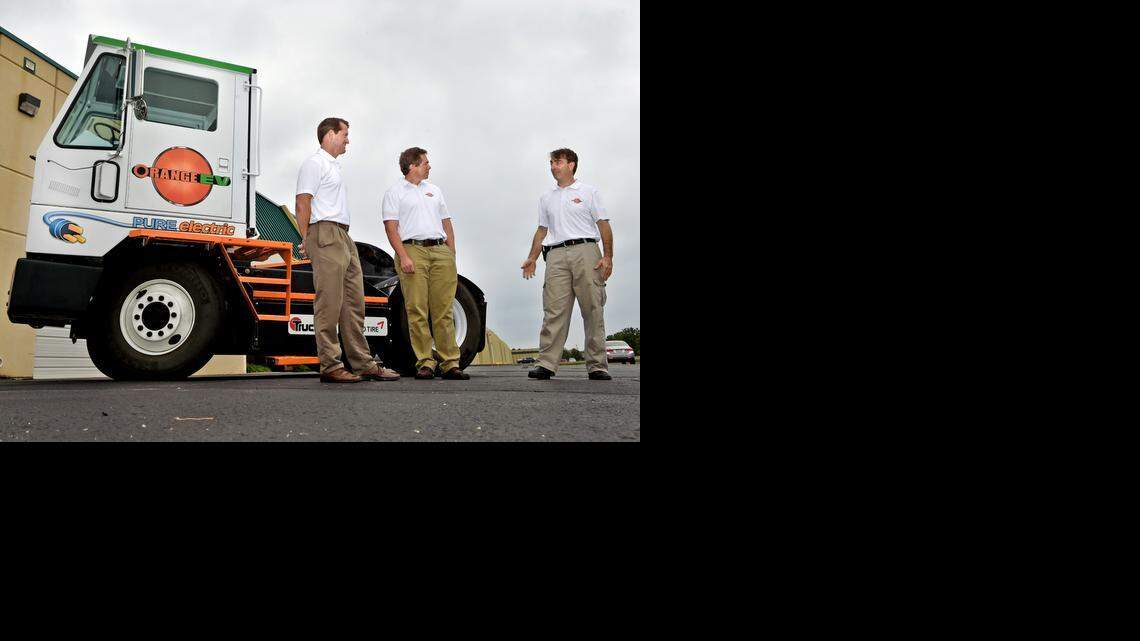 Mike Saxton (from left), Wayne Mathisen and Kurt Neutgens, all with Orange EV, conferred near one of their electric trucks at the company’s headquarters in Riverside. Orange’s trucks are former diesel models retrofitted with electric motors.