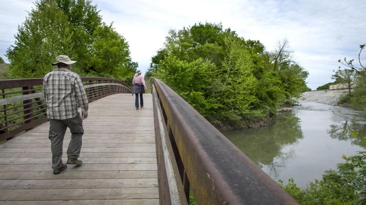 Frank and Jeanne Smith of Tonganoxie walk across the bridge to Nelson Island in Shawnee. The island serves as the northern end of the 17-mile Gary L. Haller Trail in Mill Creek Streamway Park.