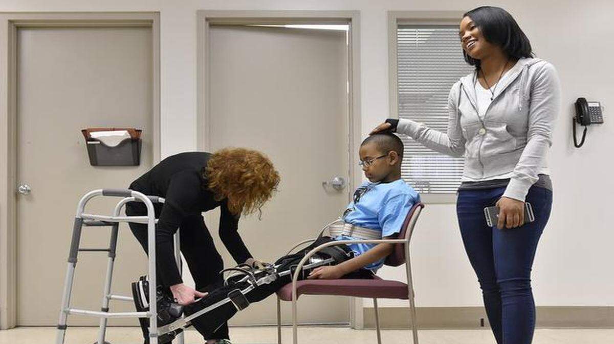 Physical therapist Michele Ahern of the Rehabilitation Institute of Kansas City adjusted the leg braces worn by 11-year-old Ka’Vyea Tyson-Curry during a recent rehab session. Tanesha Tyson gave her son encouragement.