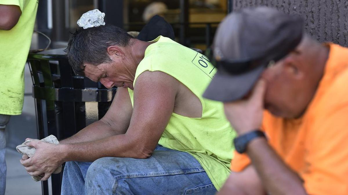 

Blacktop Paving Maintenance workers Jim McCaine (left) and Billy Gilmore, both of Kansas City, North, moved to the shade as they took a break Monday from paving the parking lot at Merriam Town Center.  McCaine used a chunk of ice on his head to get relief. The crew is expected to continue at the site for the next couple of days.
