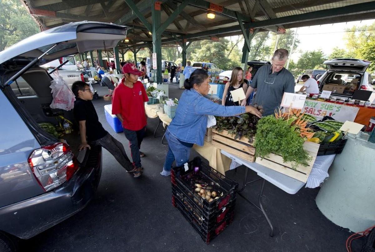 At the New Roots for Refugees stand at the Parkville Farmers Market, San Win (right, foreground) and Ah Tun help their customers.