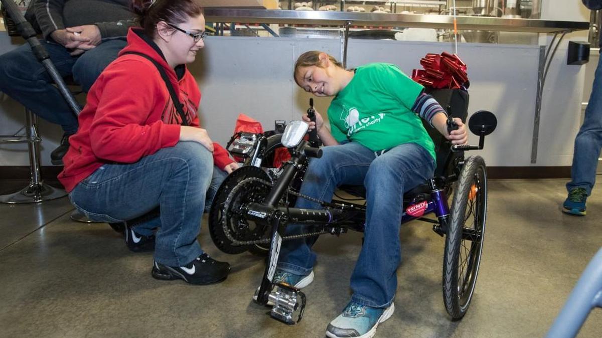 Katlynn Spooner (seated) checks out her new adaptive bike as her mom, Kelle Spooner, looks on during a surprise gift ceremony last month at The Roasterie.
