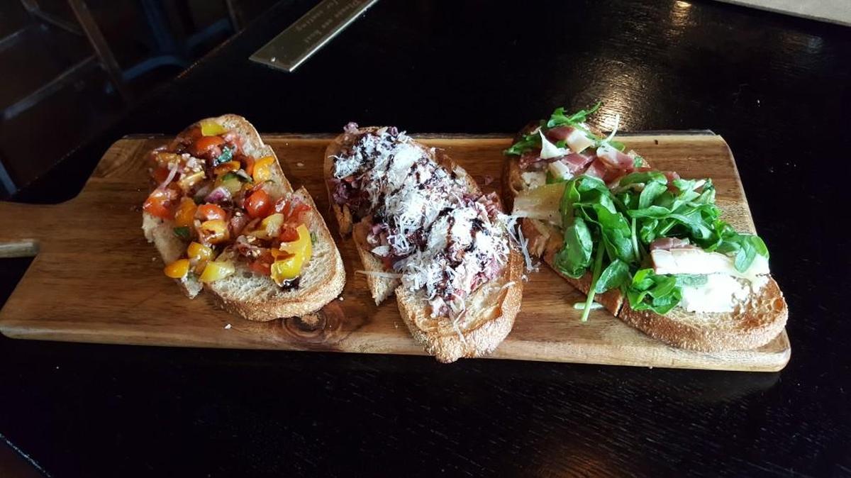 The Bruschetta Trio features dense, hearth-baked bread with three different toppings: Serrano ham; heirloom tomatoes and two-olive tapenade