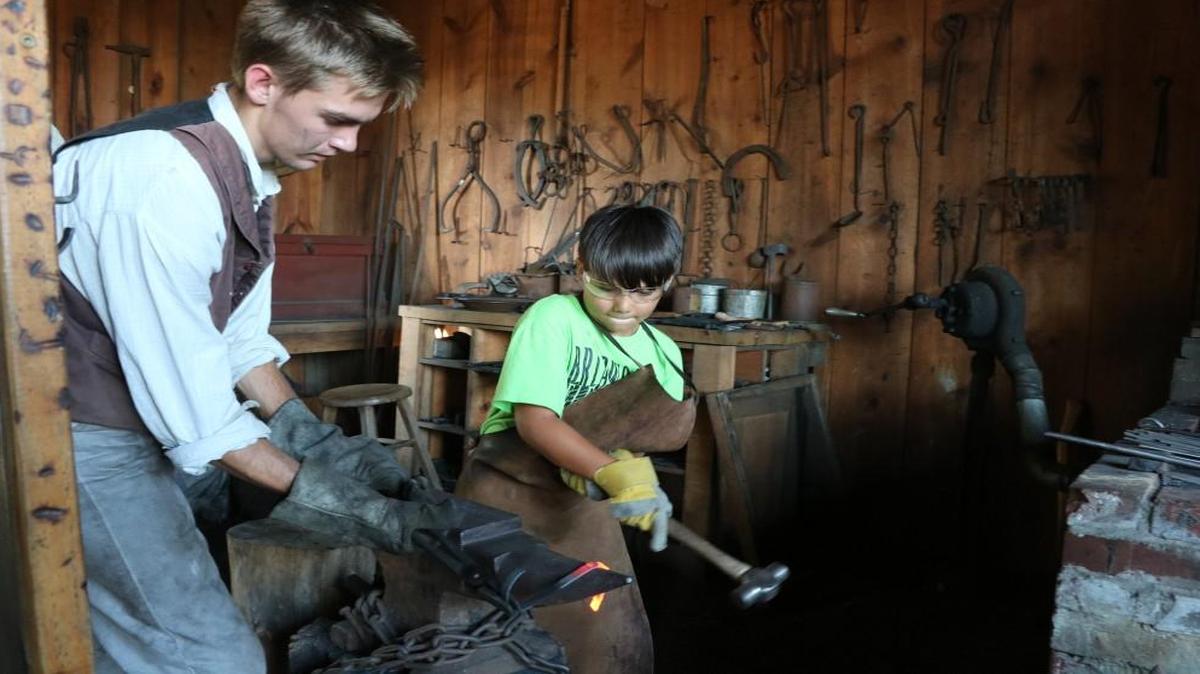 During Thursday evening’s Independence Day Family Fun Night at the Mahaffie Stagecoach Stop & Farm, Brycen Luna, 9, perfects his blacksmith skills with the guidance of blacksmith, Nicholas McCreight.