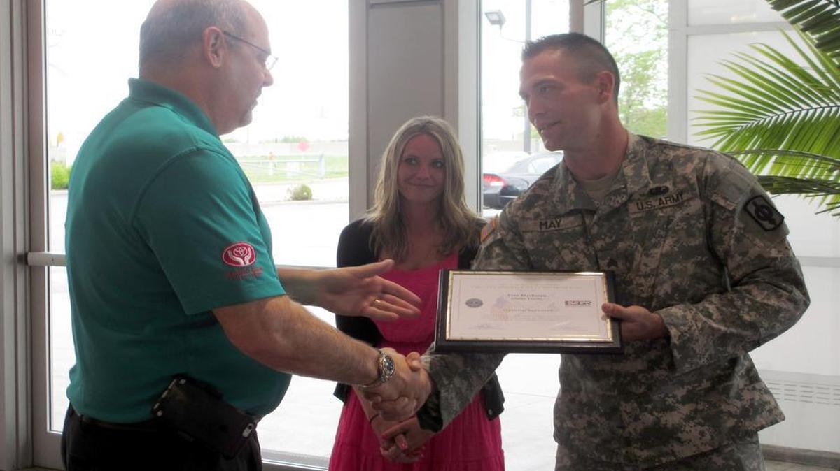 As his wife, Janelle May, looks on, Sgt. Mitchell May of the Kansas National Guard shakes hands with his supervisor at Olathe Toyota, Tom Blackman, after presenting Blackman and several others with the Service Member Patriot Award.