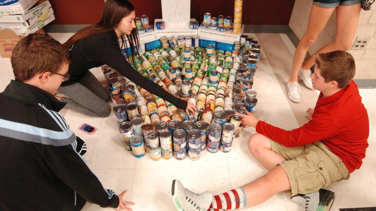 For a Week of Giving event at Olathe Northwest High School, some freshmen sculpted Kauffman Stadium out of canned goods that were later donated to the Johnson County Christmas Bureau. Sami Clark (above left) applied finishing touches to “Can-sas City Royals” with assistance from Ryan Burnett (left) and Jackson Thayer.