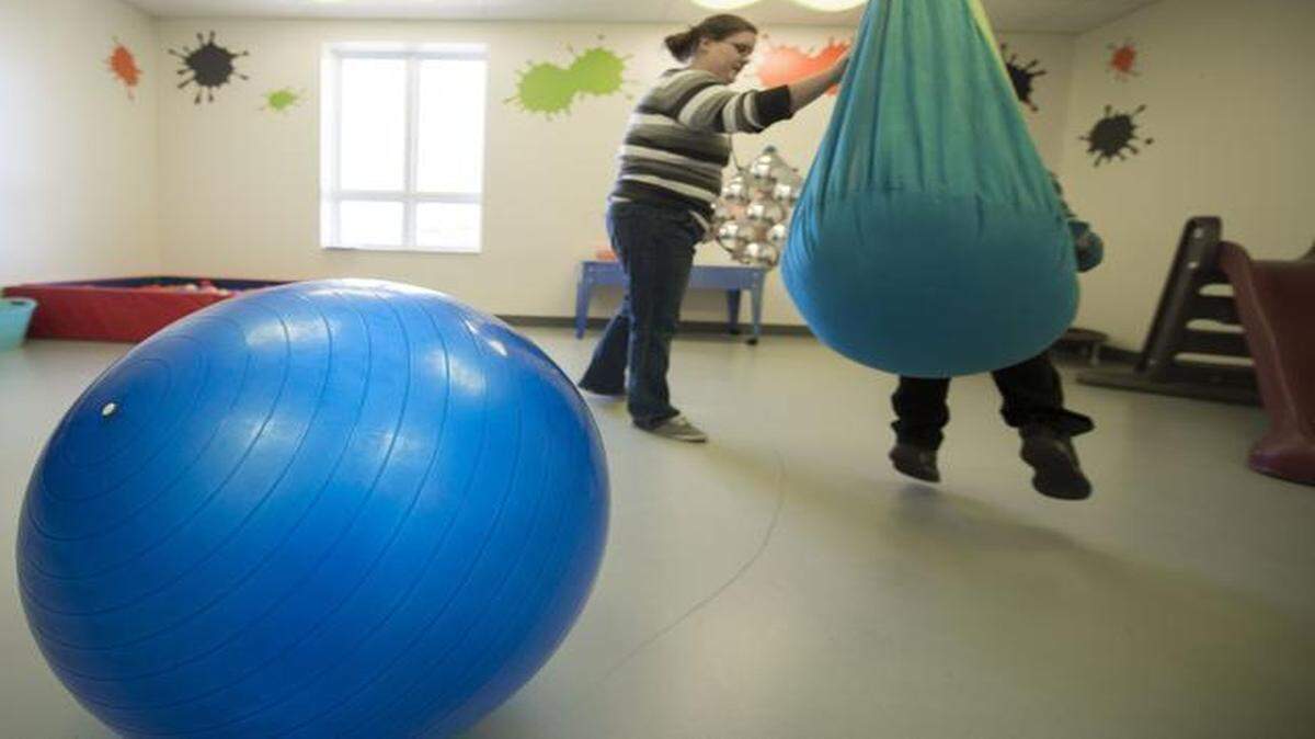 
In the gym room of the KidsTLC autism center, program facilitator Melissa Bruce steadies a hammock swing as a student sits down. 
