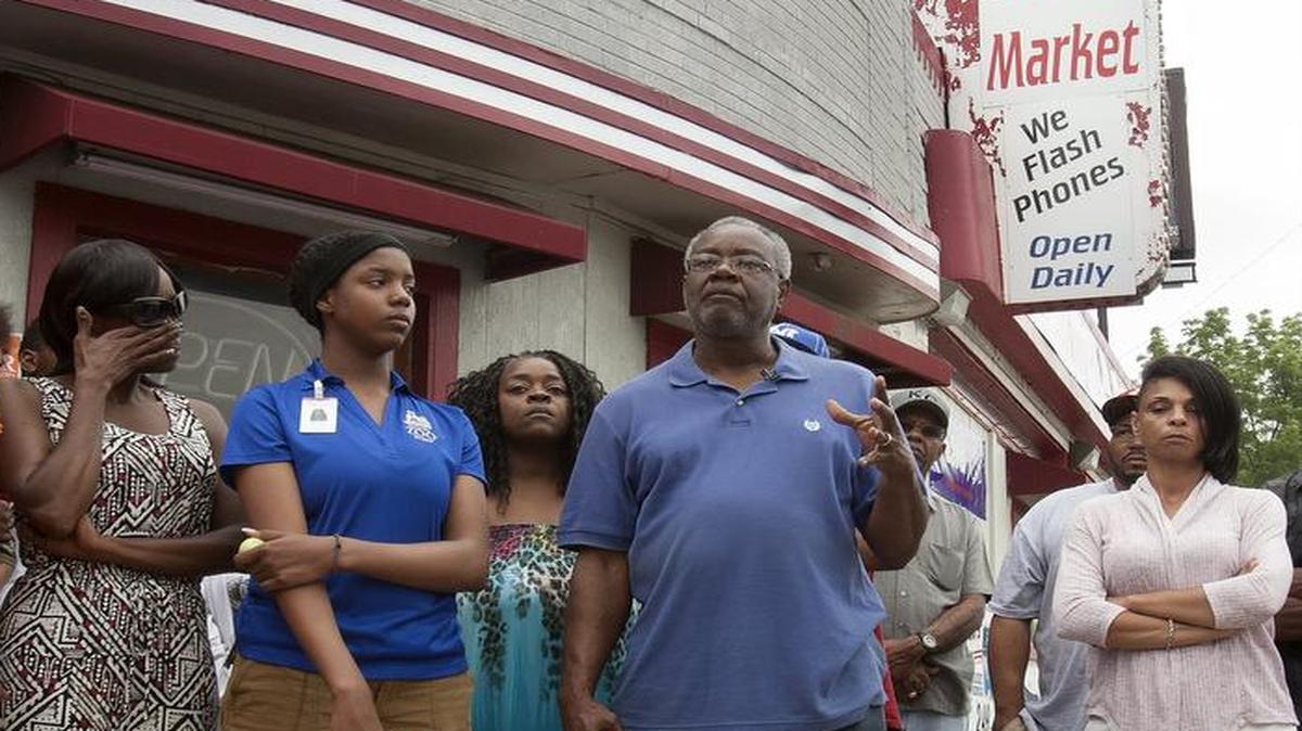 
Will Jones (center), grandfather of the 16-year-old boy who was shot Tuesday afternoon at the Pic N Save at 5846 Prospect Ave. for allegedly stealing a package of cookies, spoke to the community Thursday evening in front of the store.


