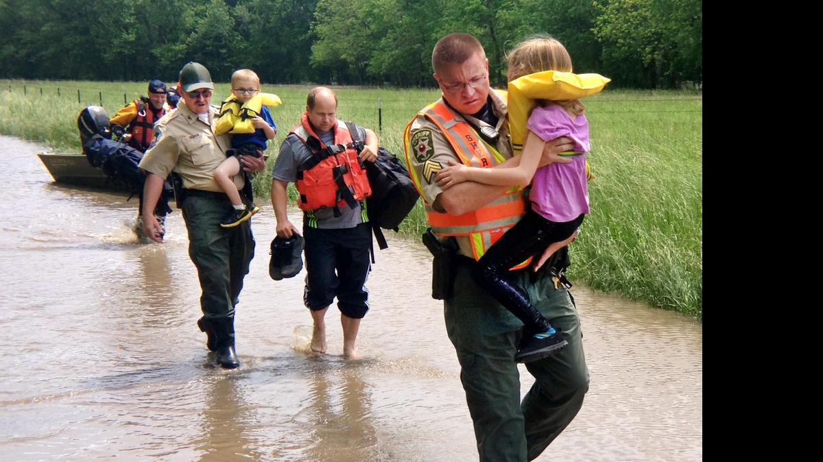 
Rescuers helped Steve Laudie (center, carrying his shoes) and two of his children Amaura, 9, and Davis, 5, through floodwaters after their Mosby, Mo., home was flooded Sunday. Heavy rains from thunderstorms Saturday night into Sunday morning caused the Fishing River near Mosby to flood. Sgt. Chris Johnson, with the Clay County Sheriff's Office, carried Amaura, while Clay County parks chief Zephry Bingham carried Davis. Missouri Highway Patrol Sgt. Bryan Parrott and Cpl. David Campbell assisted with the rescue. 
