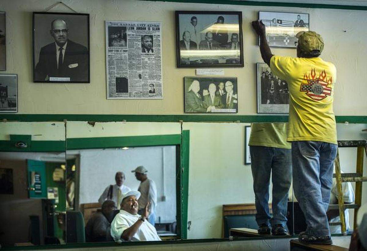 Bruce Watkins, Jr., lower center, watched Walter Allen, right, hang historical photos, including photos of former Kansas City police lieutenant and black political leader Leon Jordan, on the walls of the Green Duck Lounge and Grill at 25th & Prospect Avenue on Monday afternoon. Watkins, Jr. is coordinating a petition drive to have the future East Patrol Station next door to the Green Duck Lounge named after Jordan.