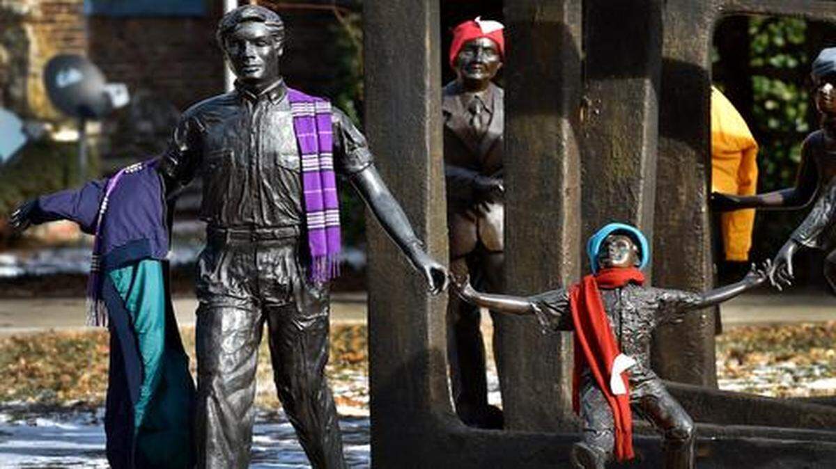 
Although it may seem funny, there is a serious side to these statues at Cancer Survivors Park adorned with winter clothing. Someone has decorated the bronze figures with winter clothing items and attached a tag that reads, “No I’m not lost, if you are in need, please take me and stay warm.” 
