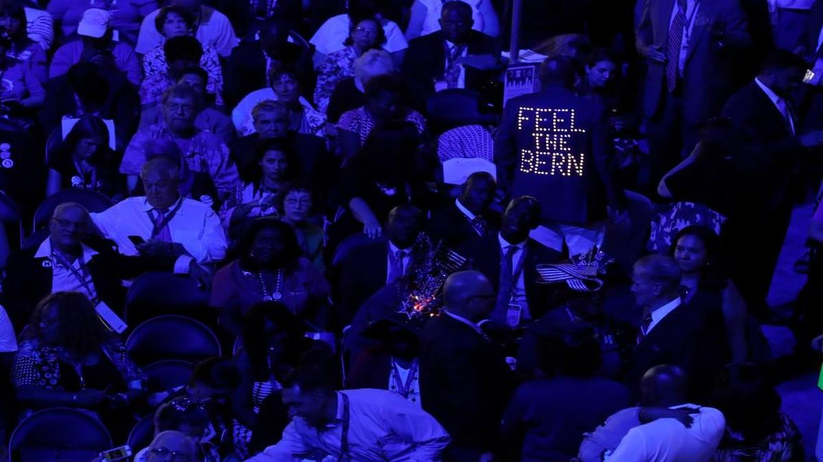 The lighted back of a Bernie Sanders supporter’s jacket stands out among the delegates during the first day of the Democratic National Convention in Philadelphia. Sanders people made clear they weren’t happy about how the primaries turned out.