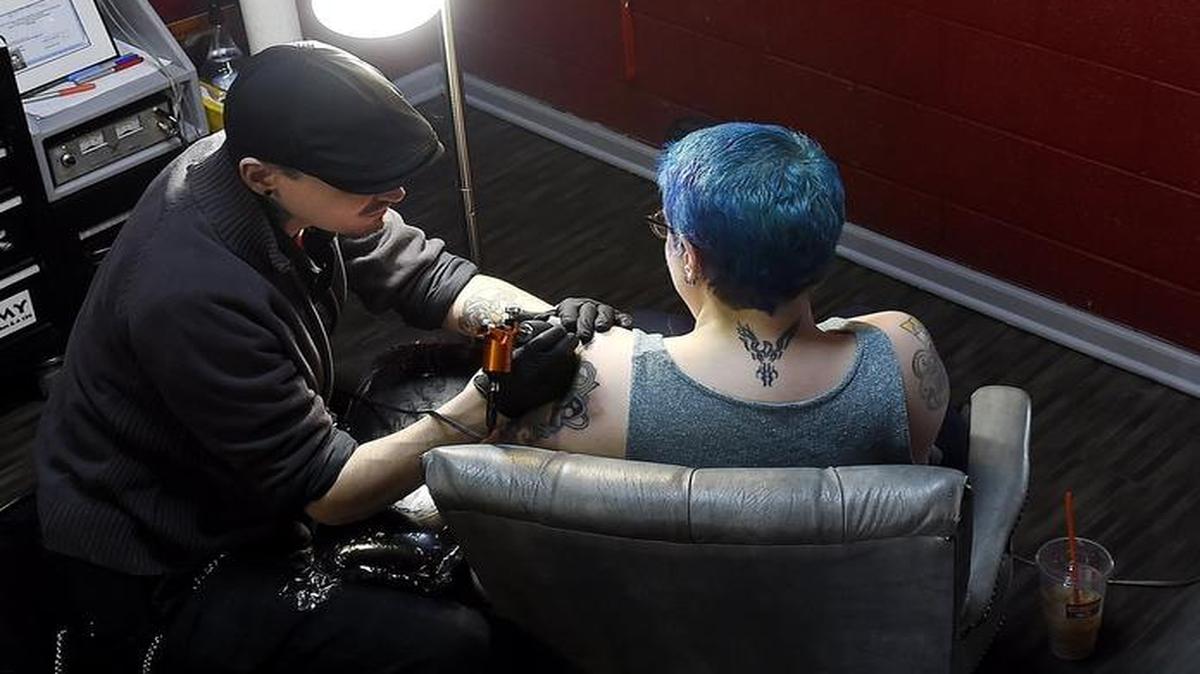 
Tattoo artist Brett Murdock (left) is offering free nipple tattoos to women who have had mastectomies. His motivation: wife Rachael Frederick, who last year, at age 32, was diagnosed with a severe and aggressive form of breast cancer and who had a double mastectomy. Murdock recently did some touchup work on a tattoo on Frederick’s shoulder.
