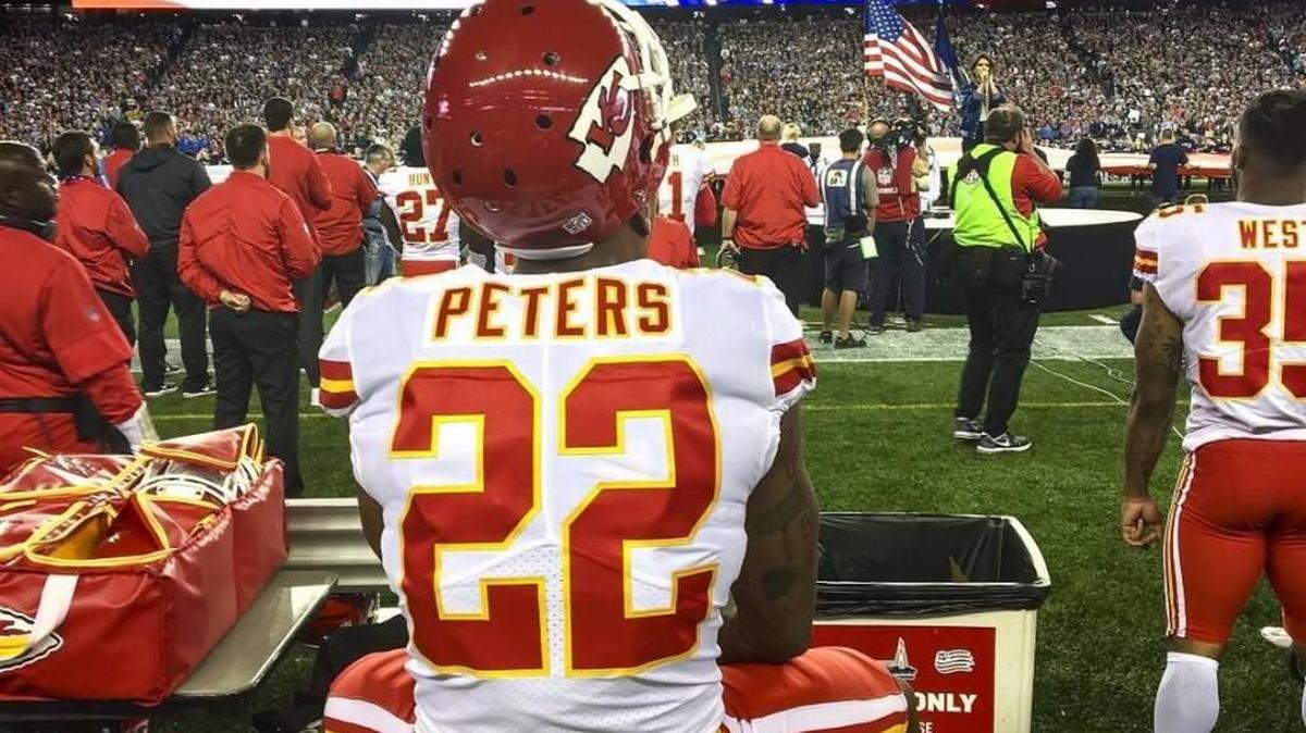 Marcus Peters sat on a trainer’s bench during the National Anthem prior to the Chiefs’ game against the New England Patriots.