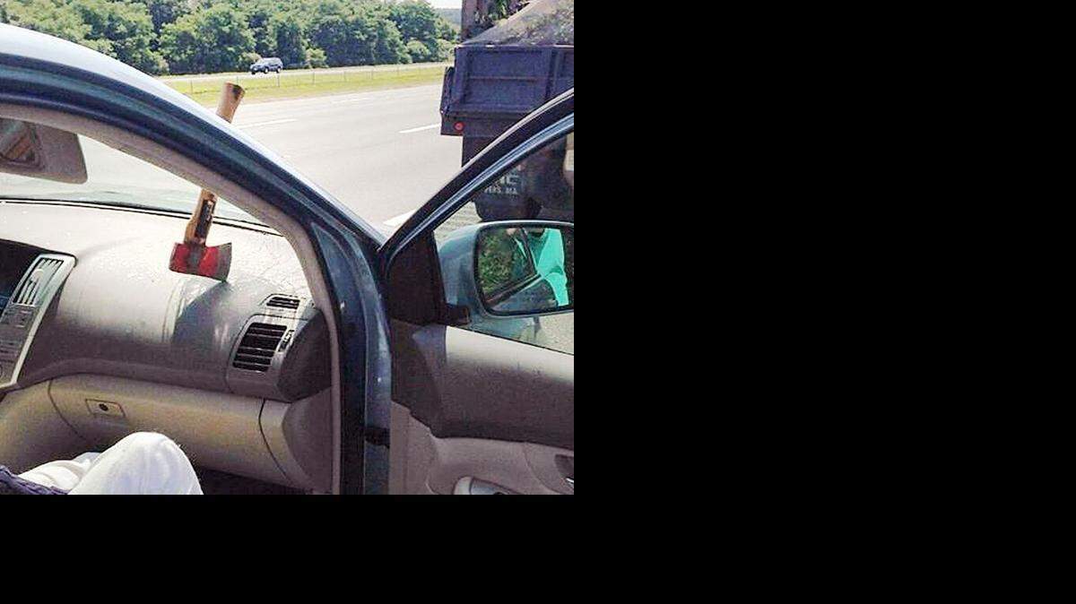 
An ax head rests on the dashboard with the handle stuck in the windshield of a driver’s car after falling off a landscaper's truck 
