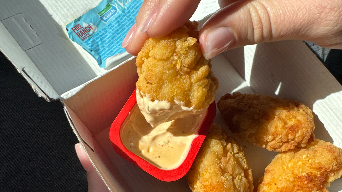 An image of a fast food chicken nugget dipped in sauce.