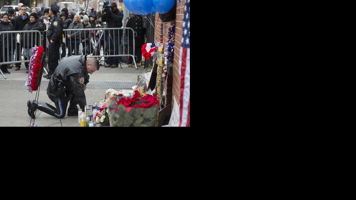 
A police officer kneels at a makeshift memorial as pedestrians look on near the site where NYPD officers Rafael Ramos and Wenjian Liu were murdered in the Brooklyn borough of New York.

