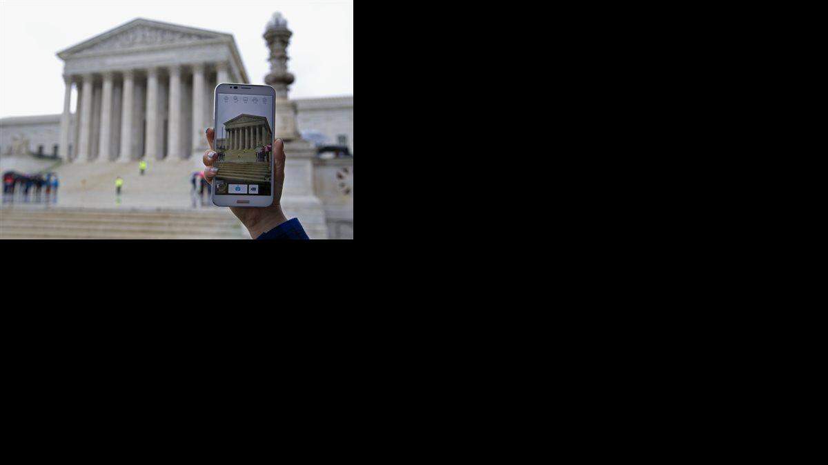 FILE - In this Tuesday, April 29, 2014 file photo, a Supreme Court visitor takes pictures with her cell phone outside the Supreme Court in Washington, during a hearing to consider whether police may search cell phones found on people they arrest without first getting a warrant. The Supreme Court ruling barring police from searching cell phones without a warrant had an immediate impact as police nationwide were briefed during roll calls, new procedures were issued and prosecutors discussed the potential impact to possibly thousands of pending court cases. From Los Angeles to New York, and in San Diego, Chicago and Houston, departments met to discuss the unanimous ruling issued Wednesday, June 25, 2014, that prohibits law enforcement from searching an arrestees’ cell phone without a warrant unless a person’s safety or life may be in danger and could make it harder for officers to quickly find incriminating evidence.