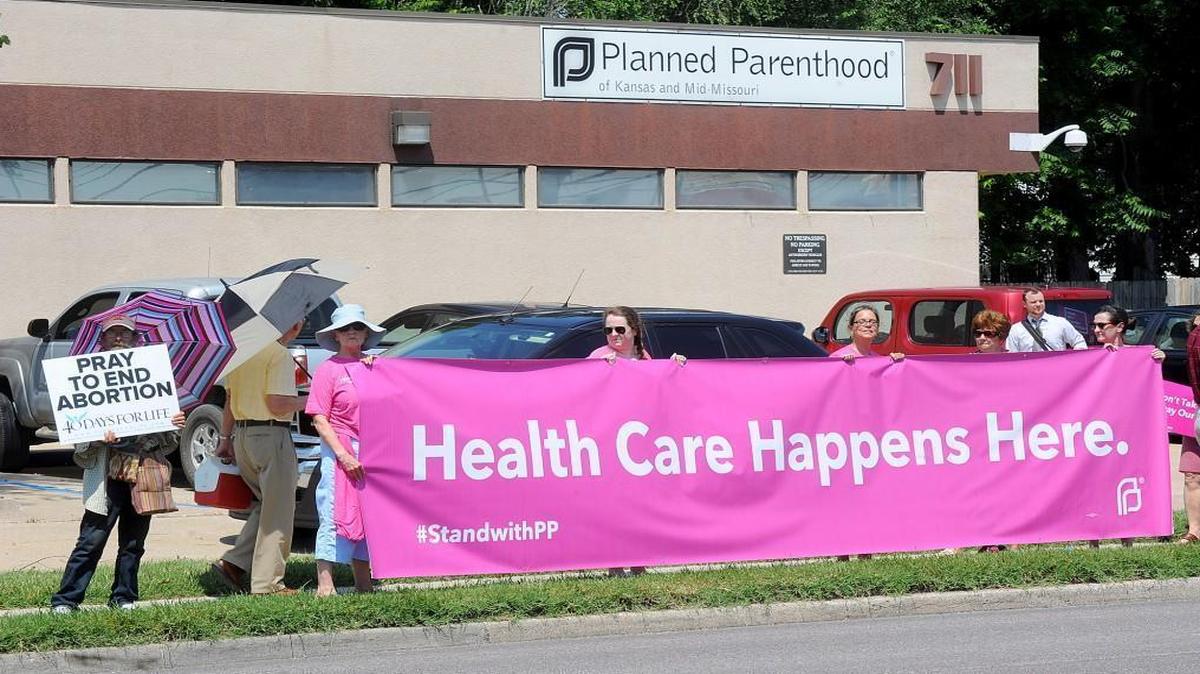 A man holding a sign who refused to give his name, left, stands next to five women holding a large banner supporting Planned Parenthood of Kansas and Mid-Missouri Tuesday, July 28, 2015, in front of Planned Parenthood in Columbia, Mo.