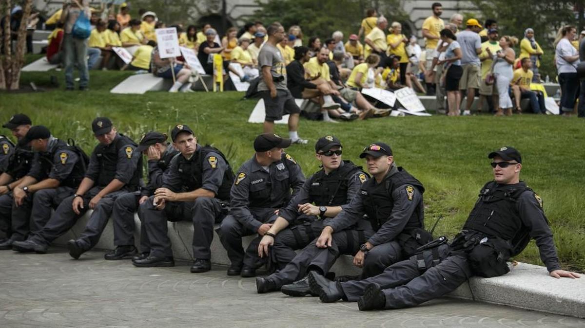 Police officers sit together as protests calm down at the Public Square on the last day of the Republican National Convention on Thursday. The protests were mostly peaceful, but authorities are investigating whether stickers that protesters handed out to police were tainted.