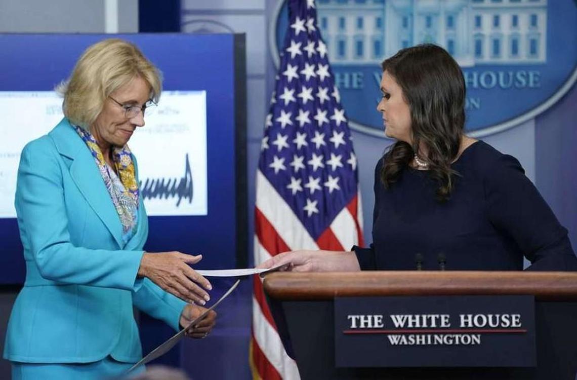 White House press secretary Sarah Huckabee Sanders, right, hands Education Secretary Betsy DeVos, left, a check signed by President Donald Trump in the Brady Press Briefing room of the White House on July 26. President Trump donated his second quarter salary to the Education Department.