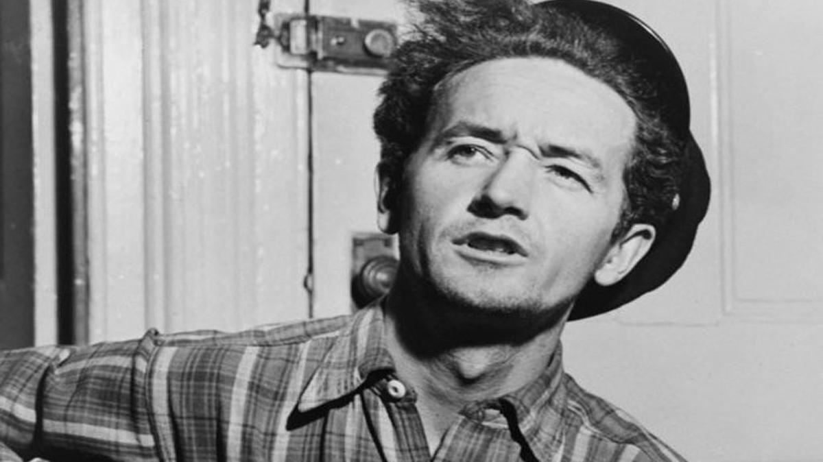 American folk singer Woody Guthrie plays his famous guitar with a sticker that says “This machine kills fascists.”
