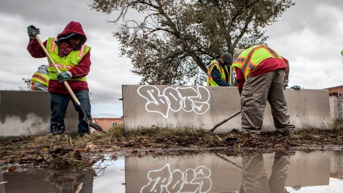 A crew of homeless people dig up weeds along a side street as part of a new program in Albuquerque, N.M. As part of an attempt to deal with rising poverty and destitution, a program pays homeless people $9 an hour for a daylong job cleaning up parts of the city.