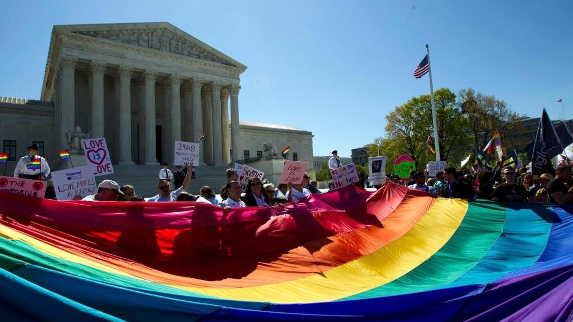 Demonstrators stand in front of a rainbow flag of the Supreme Court in Washington.