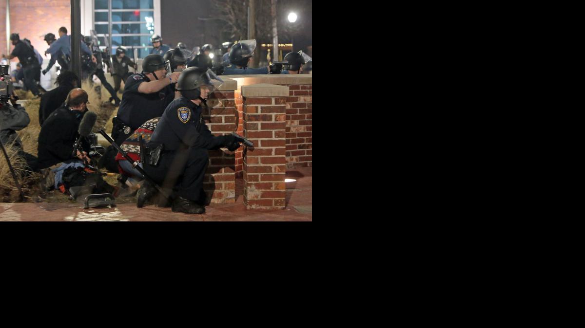 
Police take cover after two officers were shot while standing guard in front of the Ferguson Police Station on Thursday,
