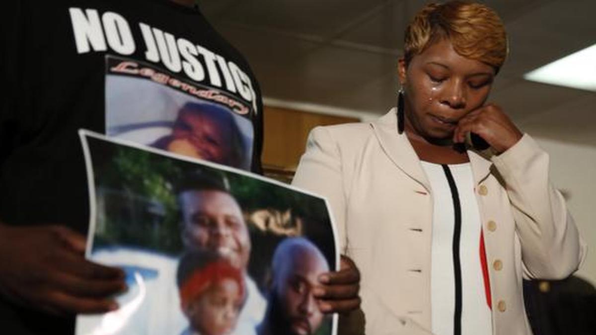 
Lesley McSpadden, the mother of 18-year-old Michael Brown, wipes away tears as Brown's father, Michael Brown Sr., holds up a family picture of himself, his son, top left, and a young child 
