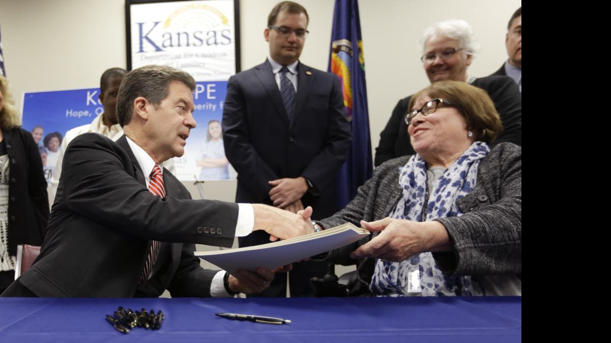 
Gov. Sam Brownback congratulates Department for Children and Families secretary Phyllis Gilmore after signing a welfare reform bill into law. A faulty provision in the law could cause Kansas to lost about $102 million in federal money.
