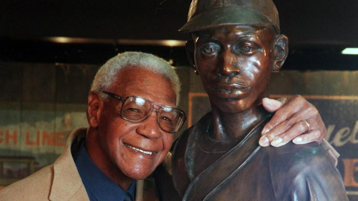 Negro Leagues legend Buck O’Neil poses in 1997 with a statue of Satchel Paige at the Negro Leagues Baseball Museum in Kansas City.