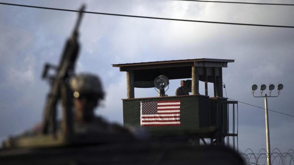 A U.S. trooper is at a machine gun in the turret on a vehicle as a guard looks out from a tower in front of the detention facility at Guantanamo Bay U.S. Naval Base, Cuba. Enemy combatants remain held there awaiting trial after the Sept. 11, 2001, terrorist attacks.