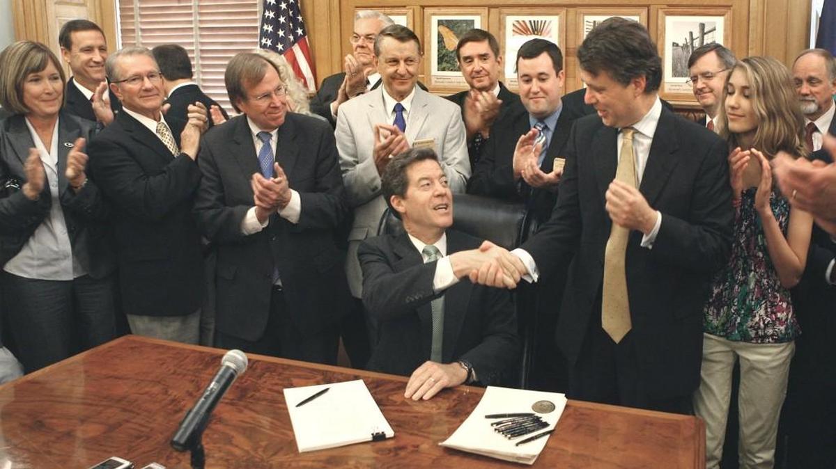 On May 22, 2012, Kansas Gov. Sam Brownback (seated) signed into law income tax cuts that have slashed state revenues by hundreds of millions of dollars a year.