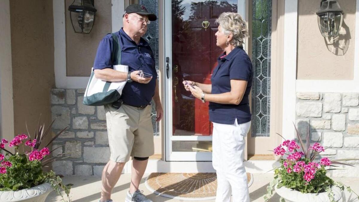John Skubal (left) talked with Amy Newsum, a Blue Valley Northwest school teacher, on her front porch in June. Skubal, a Republican, is running for the 11th District Kansas Senate seat.