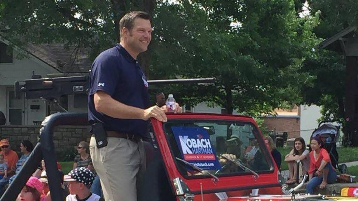 Kris Kobach rode in a Jeep during the Old Shawnee Day Parade with a large gun replica mounted in back.