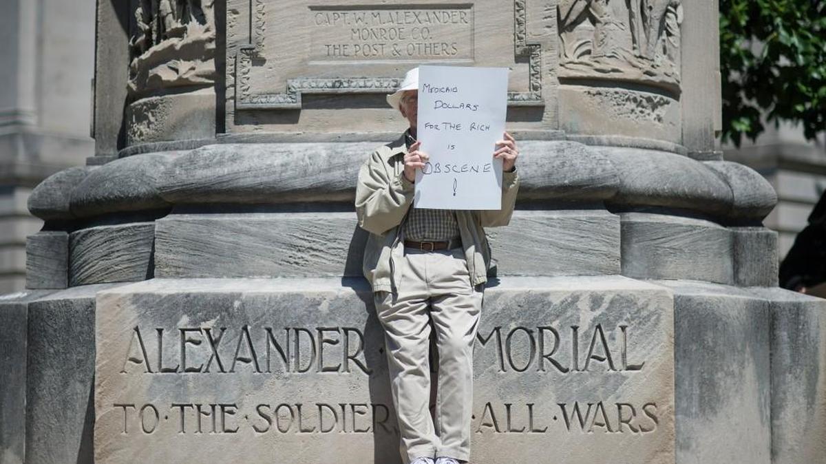Gates Agnew holds a sign reading “Medicaid Dollars for the Rich is Obscene” as he and others gathered to protest the current health care bill being considered in the Senate with a “die-in” at the Monroe County Courthouse in Bloomington, Ind. Monday, June 26.