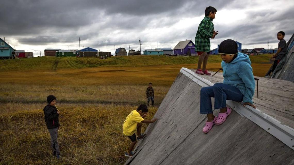 Children play on the weathered plywood sides of an enclosure in the Alaskan village of Shaktoolik, Sept. 18, 2016. Laid out on a narrow spit of sand between the Tagoomenik River and the Bering Sea, the village is facing an imminent threat from increased flooding and erosion, signs of a changing climate.