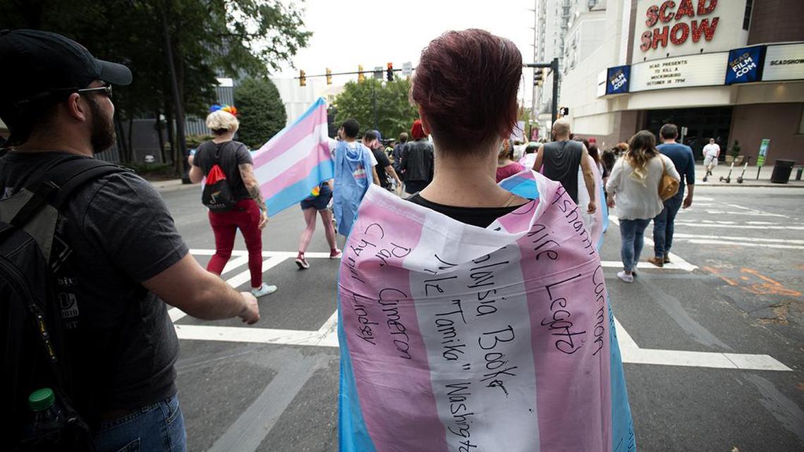 A supporter for the transgender and non-binary community, wearing a transgender flag with handwritten names of black trans women who the person said were killed in 2019, strolls through the city’s Midtown district during Gay Pride Festival’s Transgender Rights March in Atlanta on Saturday, Oct. 12, 2019. The march was part of the annual Gay Pride Festival. (AP Photo/Robin Rayne)