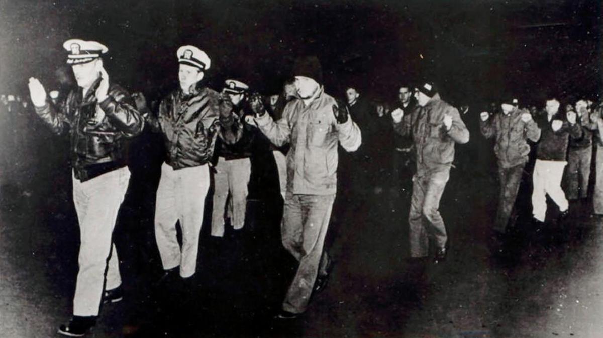 In this photo released by the U.S. Navy, crew members of the USS Pueblo hold up their hands while in captivity in North Korea in 1968.