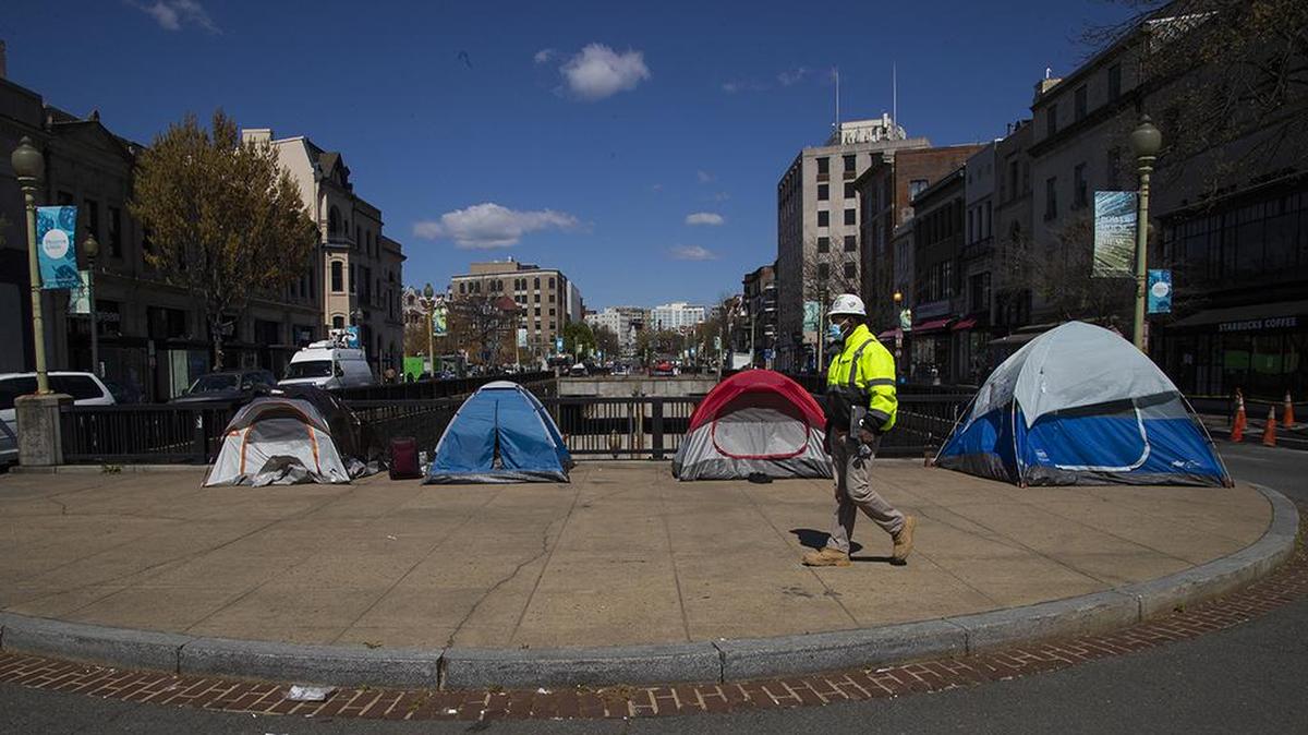 A street maintenance subcontractor for the District of Columbia walks past tents set up by the homeless on a sidewalk in Washington’s Dupont Circle.