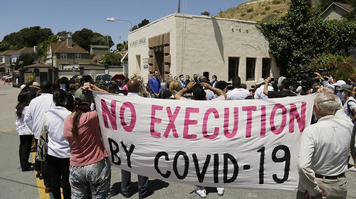 FILE - In this July 9, 2020, file photo, people hold up a banner while listening to a news conference outside San Quentin State Prison in San Quentin, Calif. The group of legislators, advocates, academics and public health officials gathered outside San Quentin State Prison to discuss a COVID-19 outbreak at the facility that has sickened more than 1,400 inmates with six deaths. California’s workplace safety regulator has ordered the dental clinic at San Quentin State Prison to stop many of its operations due to practices it says contributed to the spread of COVID-19 at the facility, the San Francisco Chronicle reported Thursday, Sept. 3, 2020. (AP Photo/Eric Risberg, File)