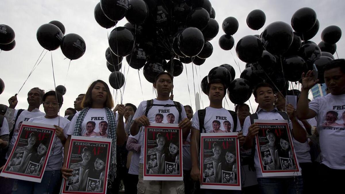 Activists holding signs with the Time Magazine cover showing wives of two Reuters journalists stand during a rally to mark one year anniversary of their arrest, Wednesday, Dec. 12, 2018, in front of city hall in Yangon, Myanmar.